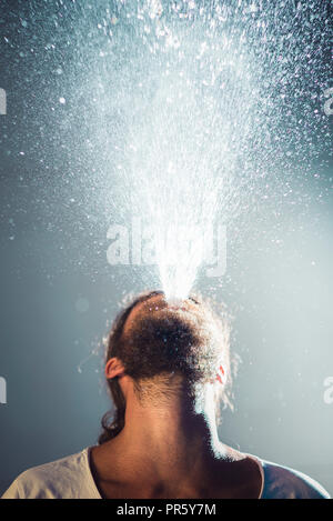 Junger Mann bläst das Wasser aus dem Mund Stockfoto