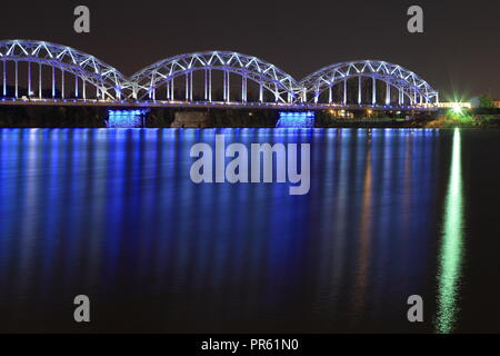 Eisenbahn Brücke überquert den Fluss Daugava in Riga (Lettland) in der Nacht. Letten feiert 100 Jahre Unabhängigkeit während des ganzen Jahres 2018. Stockfoto