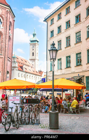 München, Deutschland - Mai 8, 2013: Fahrräder und Leute an Street Cafe in der Altstadt von München. Heiliggeistkirche auf dem Hintergrund Stockfoto