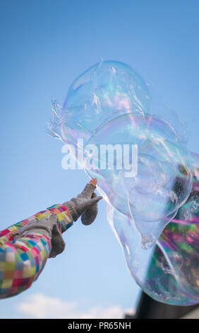 Mädchen, die sich ihre Hand, die versuchen, die riesige Seifenblasen schweben hoch in die Luft mit dem blauen Himmel im Hintergrund zu berühren Stockfoto