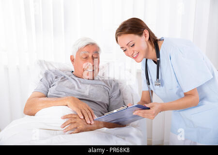 Junge weibliche Krankenschwester mit Zwischenablage Besuchen ältere männliche Patienten Stockfoto