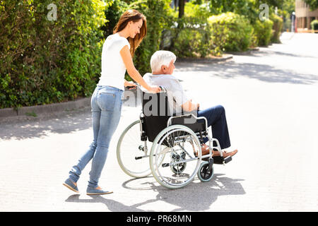 Junge Frau bei ihrem behinderten Vater auf Rollstuhl an im Freien Stockfoto