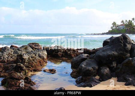 Kleine Wellen auf einem vulkanischen Felsen in Paia Bay, Maui, am Anfang der Straße nach Hana Stockfoto