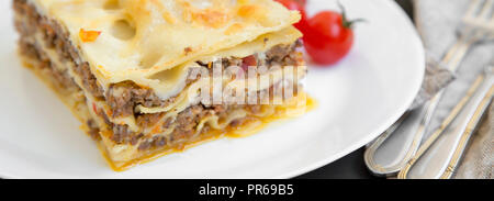 Traditionelle Rindfleisch Lasagne auf eine weiße, runde Platte auf schwarz Tabelle, Seitenansicht. Close-up. Stockfoto