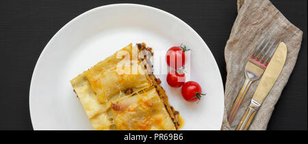 Traditionelle Rindfleisch Lasagne auf eine weiße, runde Platte auf schwarzen Hintergrund, Ansicht von oben. Close-up. Stockfoto