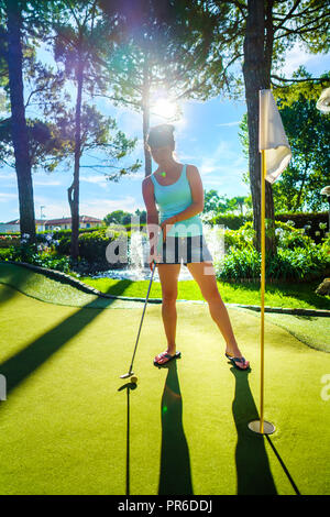 Mini Golf - Frau Golf spielen auf grünem Gras bei Sonnenuntergang Stockfoto