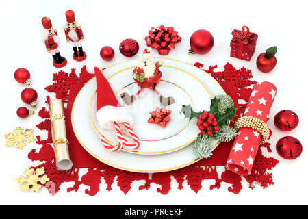 Weihnachtsessen spaß Tisch mit Porzellan Teller, Christbaumkugel Dekorationen, Serviette, winter Stechpalme Tanne und auf einem roten Unterlage auf weißem Hintergrund. Stockfoto