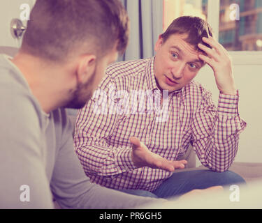 Gestörte Mensch, ernstes Gespräch mit seinem Freund auf dem Sofa zu Hause Stockfoto