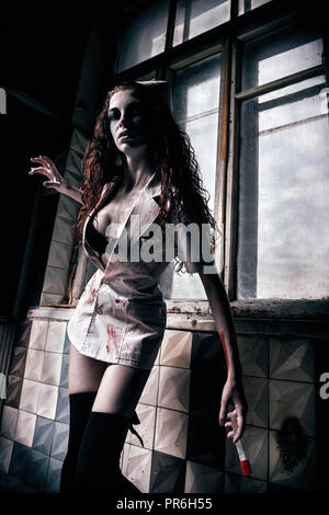 Horror geschossen: Die creepy Evil mad Nurse (Arzt) mit blutigen Spritze in der Hand. Zombie Frau (lebende Tote) Stockfoto