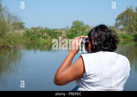 53 Jahre alte asiatische Frau an der Vorderseite eines Kanu seitwärts drehen nach links durch ein Fernglas für wilde Leben sitzen, das Kanu ist Stockfoto