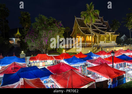 Night Market und beleuchtete Haw Pha Bang Tempel, auch als Royal oder Schlosskapelle, neben dem königlichen Palast in Luang Prabang, Laos bekannt, in der Dämmerung. Stockfoto