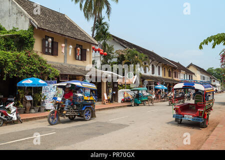 Fahrrad, Roller und zwei farbenfrohe Dreirad Taxi genannt Jumbo (oder Tuk Tuk) auf dem Sisavangvong Straße in Luang Prabang, Laos, an einem sonnigen Tag. Stockfoto