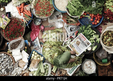 Frau liest Zeitung unter ihr Obst und Gemüse auf Siti Khadijah Markt in Kota Bharu, Malaysia. Stockfoto