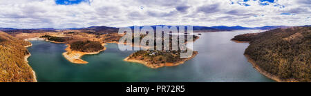 See am Lake Jindabyne Snowy River von Damm durch die Stadt Vorstädten angesichts von weit entfernten schneebedeckten Berge in erhöhten Antenne Wide Panorama. Stockfoto