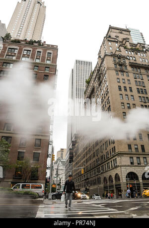 Fußgänger mit einem Zebrastreifen an der Kreuzung der Park Avenue und West 57th Street in an einem verregneten Morgen in New York City. Stockfoto