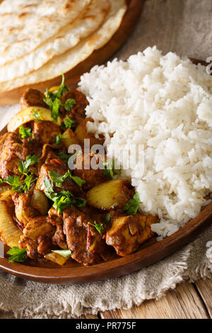 Köstliches indisches Huhn do pyaza (dopiaza) mit Zwiebeln und Garnieren von Reis close-up auf einem Teller mit Fladenbrot auf einem Tisch. Vertikale Stockfoto