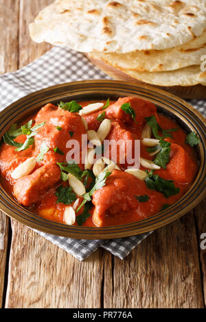 Indian Butter Chicken Murgh Makhani mit pikanter Sauce, Mandeln und Koriander close-up auf dem Teller serviert mit Brot naan auf dem Tisch. Vertikale Stockfoto