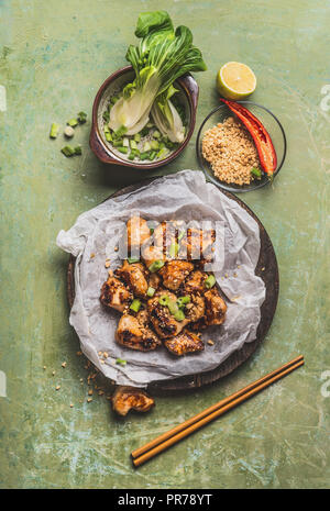 Fried Chicken Stücke mit Erdnussbutter und Frühlingszwiebeln in Papier auf Tisch Hintergrund mit Zutaten und Stäbchen. Asiatische Lebensmittel Konzept Stockfoto