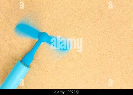 Die blauen tragbarer Ventilator ist in der blauen Power Bank und liegt auf dem Sand eingefügt. Ansicht von Oben. Stockfoto