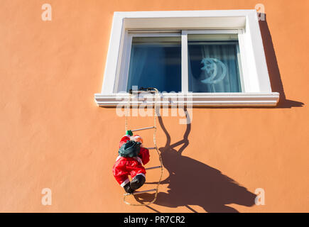 Santa Claus Klettern auf einer Wand in einem Fenster. Traditionelle Weihnachten Dekoration Stockfoto