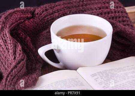 Tasse heißen Tee und Buch öffnen und Lila retro Schal auf dem Schreibtisch. Herbst Retro und Vintage Konzept. Close Up, selektive konzentrieren. Stockfoto