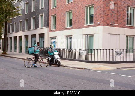 London, UK, 30. September 2018: zwei Deliveroo Lieferung Mitfahrer auf einem Fahrrad die anderen auf dem Moped in eine Diskussion, an der Kreuzung von Leigh Street und Sandwich Street in London UK. Martin Parker/Alamy leben Nachrichten Stockfoto