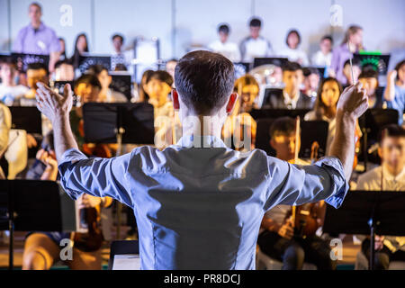 Männliche Schule Dirigent conductiong sein Schüler Band Musik in einer Schule Konzert durchführen Stockfoto