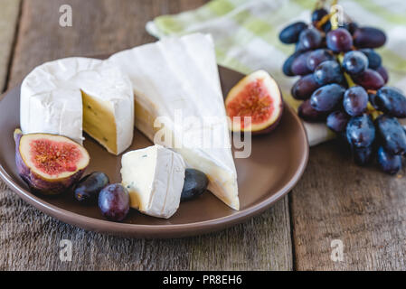 Käse mit Feigen und Trauben auf Holztisch. Stockfoto