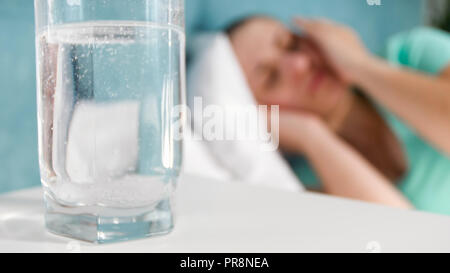 Glas Wasser mit gelösten Aspirin gegen Frau im Bett liegen und leiden unter Kopfschmerzen. Stockfoto
