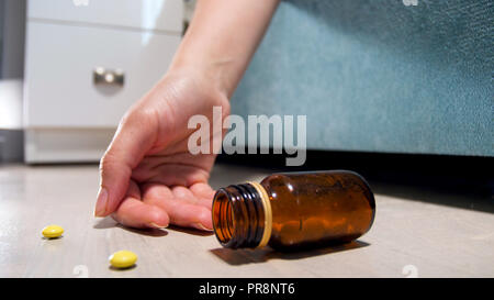 Closeup Bild der weiblichen Hand und Pillen lag auf dem Boden im Schlafzimmer. Drogensucht. Überdosierung von Betäubungsmitteln oder Medikamenten. Der Tod des Patienten Stockfoto