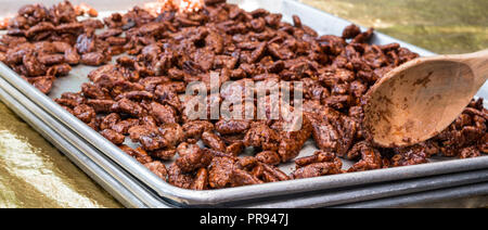 Foto von einem Löffel aus Holz und frische Zucker Zimt glasiert gebratene Pekannüsse auf ein Metall Cookie Blatt. Stockfoto