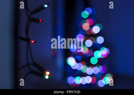 String der Weihnachtsbeleuchtung an der Wand hängen, mit Defokussierten Xmas Tree im Hintergrund. Weihnachtsbeleuchtung bokeh lifestyle Hintergrund. Stockfoto