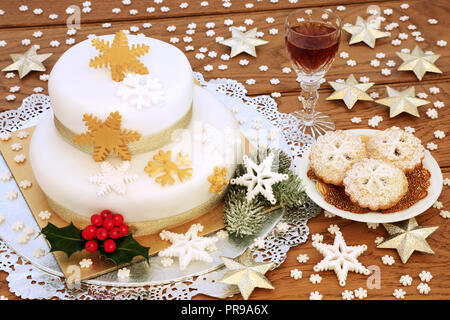 Christmas Cake mit Mince Pies und einem Glas Sherry mit Schneeflocke Dekorationen, gold Sterne, winter Stechpalme Tanne und Eiche rustikal im Hintergrund. Stockfoto