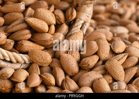 Makro von gesunden organischen Mandeln in der Schale full frame Bild mit einem alten Weidenkörbe mit selektiven Fokus im Hintergrund und Vordergrund zu Ad Stockfoto