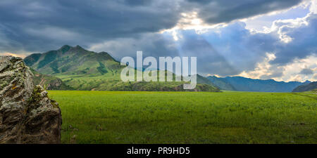Kurze Darstellung der Sonnenstrahlen Hinter düsteren Wolken über dem Tal, Altai Gebirge, Russland. Majestic Panorama Sommer Berg Sonnenuntergang Stockfoto