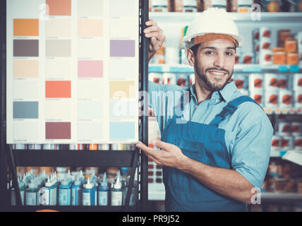 Gewöhnliche Vorarbeiter in blauen Overalls mit Proben von Farbe auf Stand in Store Stockfoto