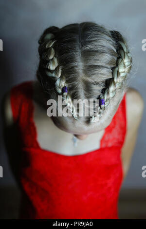 Zwei Zöpfe auf dem Kopf eines Mädchens in einem roten Kleid auf einem weißen Hintergrund, Haar close-up mit einer Verflechtung von künstlichen Materialien Stockfoto