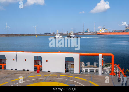 Anzeigen von zwei Schleppern, Windenergieanlagen und das Stahlwerk von Deck aus einer orange Schiff in den Hafen von IJmuiden, Niederlande. Stockfoto