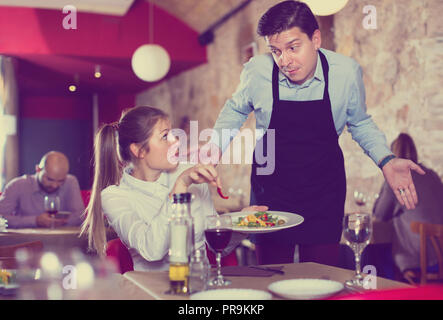 Unzufrieden unzufrieden aggressive junge Frau im Konflikt mit apologetischen Kellner wegen der schlechten Qualität der Speisen im Restaurant Stockfoto