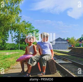 Adorable kleine Kinder auf dem Bahnhof und warten auf den Zug mit Vintage Koffer. Reisen, Urlaub und chilhood Konzept. Reiseversicherung Konzept. Urlaub Reise Stockfoto