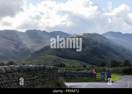 Eine hillwalker Rückkehr aus den Bergen nach dem Abstieg der Band mit Crinkle Crags Bowfell auf der linken und auf der rechten Seite. Great Langdale, Lake District, Cu Stockfoto