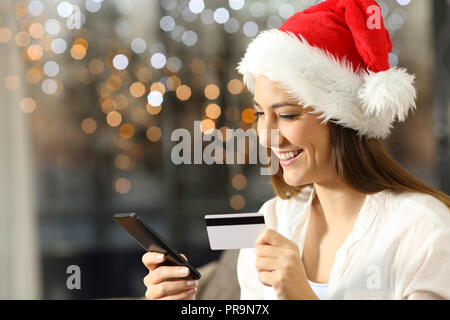 Mädchen Bezahlung Online mit Kreditkarte und Smart Phone in Weihnachten in der Nacht auf einer Couch im Wohnzimmer zu Hause sitzen Stockfoto
