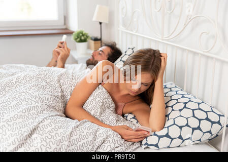 Junges Paar mit Smartphones in ihrem Bett. Schlechte Beziehung Konzept Stockfoto