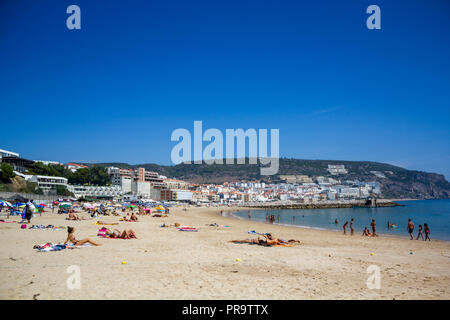 SESIMBRA, PORTUGAL - ca. September, 2018: die Menschen am Strand mit Dorf auf dem Hintergrund Stockfoto