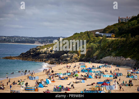 Touristischen Attraktion am Strand Stadt St Ives in Cornwall, England, Urlauber auf deackchais auf dem Sand Strand als lokaler Zug kommt auf der Stockfoto