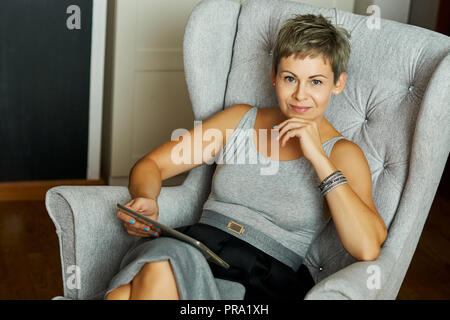 Schöne business Frau sitzt auf einem Stuhl und arbeitet auf einem Tablet-PC im Heimbüro Stockfoto