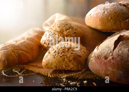 Verschiedene Arten von Brot auf sack Tuch auf einem schwarzen Holztisch in der Küche. Vorderansicht. Horizontale Zusammensetzung Stockfoto