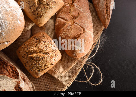 Verschiedene Arten von Brot auf sack Tuch auf einem schwarzen Holztisch in der Küche. Ansicht von oben. Horizontale Zusammensetzung Stockfoto