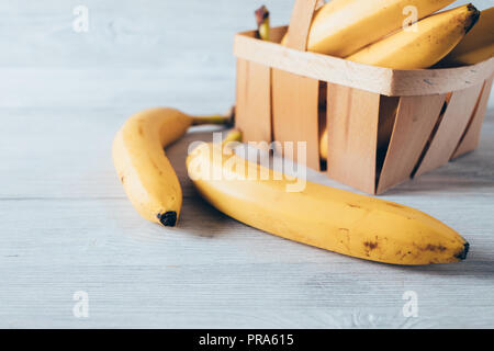 Close-up gelbe Bananen im Warenkorb und auf weisse Holztisch. Tropische Früchte mit wenig dunkle Stellen ihre Süße anzeigen Reif. Stockfoto