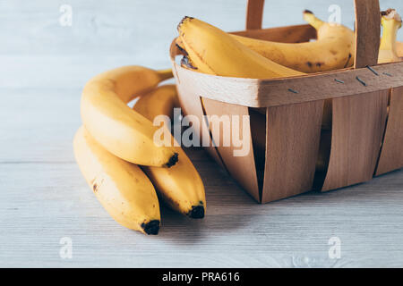 Gelb reife tropische Früchte mit wenig dunkle Stellen ihre Süße angezeigt. Close-up Bio-bananen im Warenkorb und auf weisse Holztisch. Stockfoto